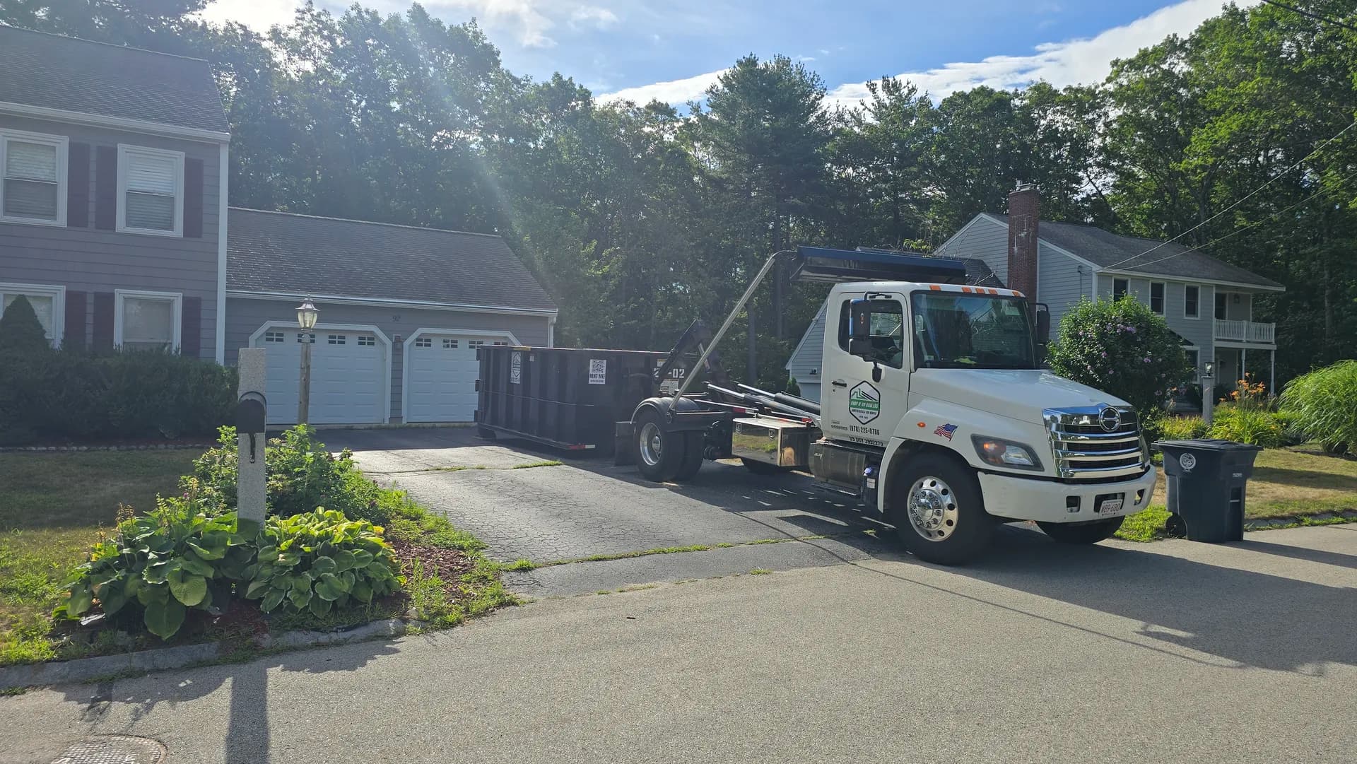 Drop N' Go Haulers truck delivering a roll-off dumpster to a suburban Colonial driveway