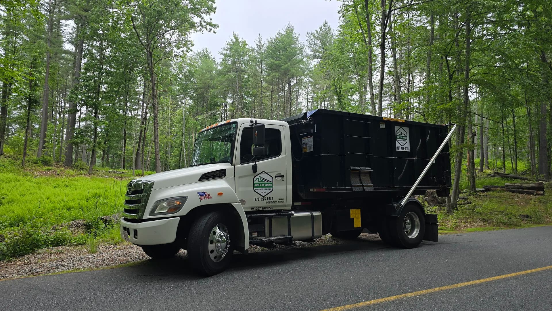 Branded truck and roll-off on a wooded New England road