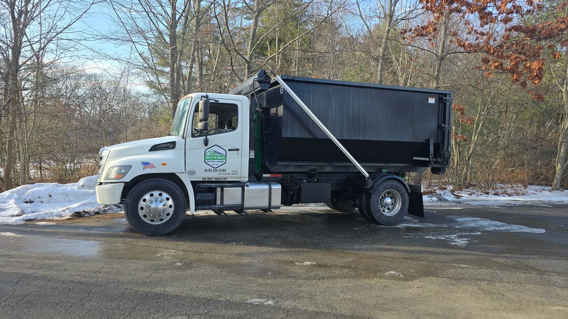 Truck delivering a roll-off to a plowed residential driveway in winter